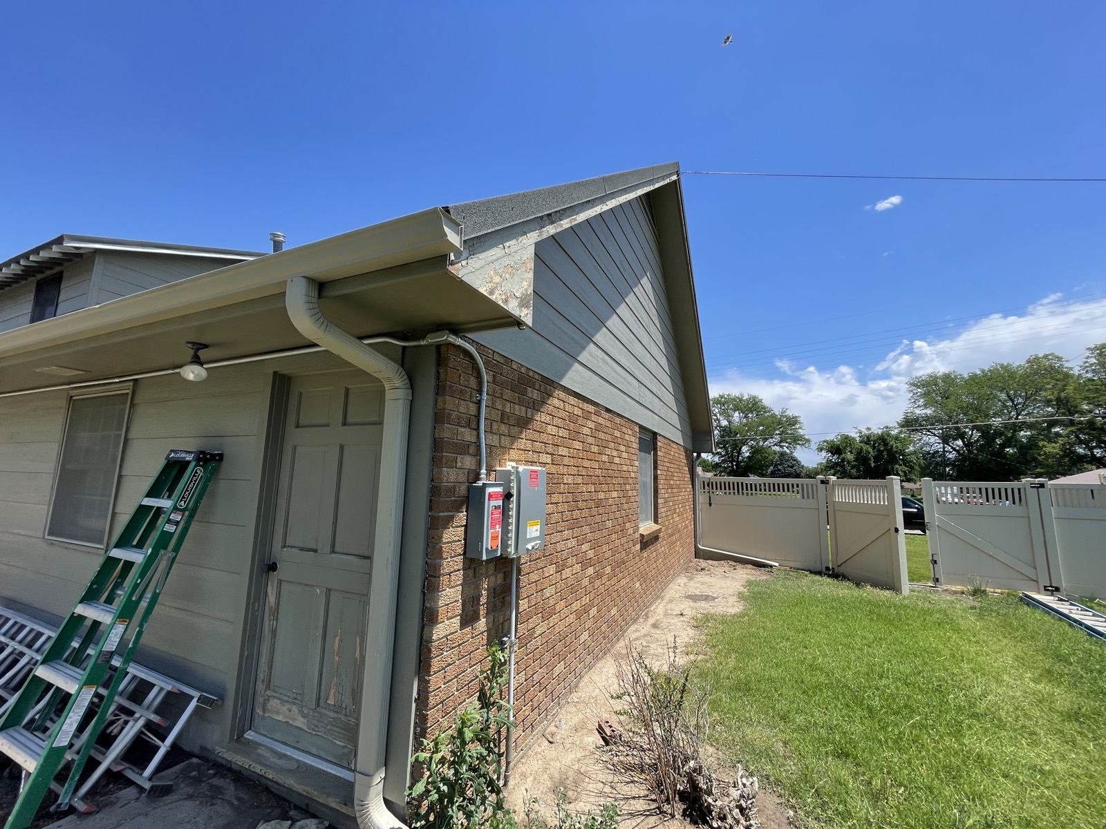 Before: patchy gable siding mid-prep with ladders